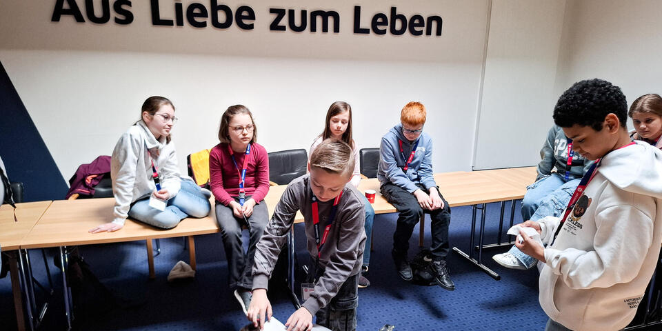 Ein Junge legt einem anderen einen Verband auf dem Kopf an. Andere Kinder schauen zu. 