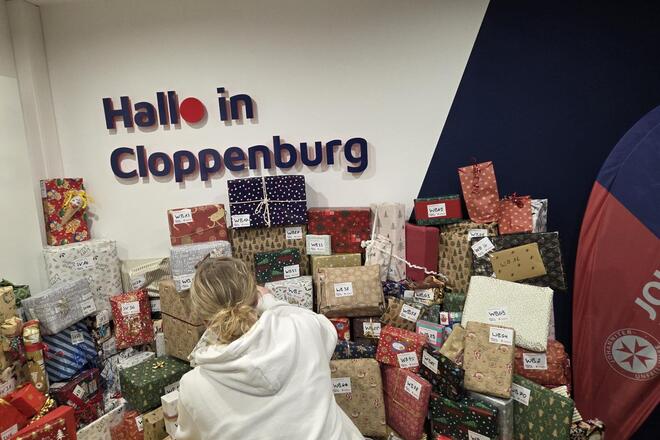 Ein Berg Geschenke in Weihnachtspapier, der von einer jungen Frau sortiert wird.