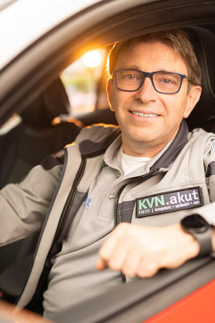 Ein Fahrer im ärztlichen Bereitschaftsdienst sitzt in einem Fahrzeug und schaut in die Kamera.