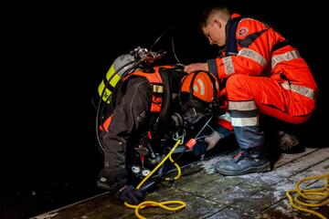 Ein Taucher steigt bei Dunkelheit ins Wasser hinab. Ein Ehrenamtlicher der Johanniter hilft ihm dabei.
