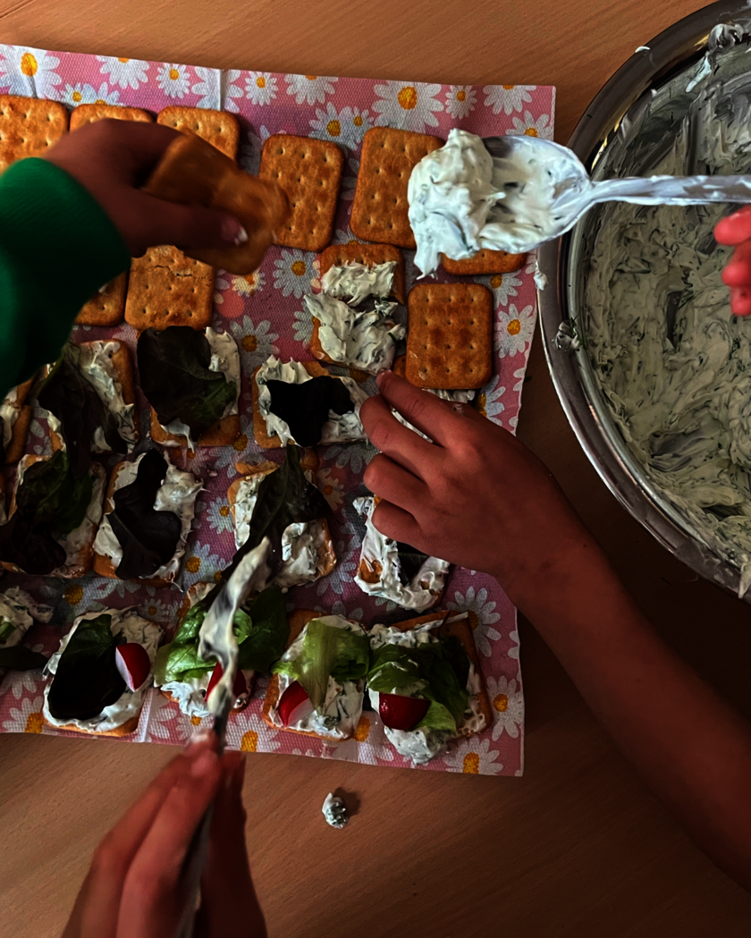 Kräuterquark aus Schüssel wird auf Kräcker verteilt.