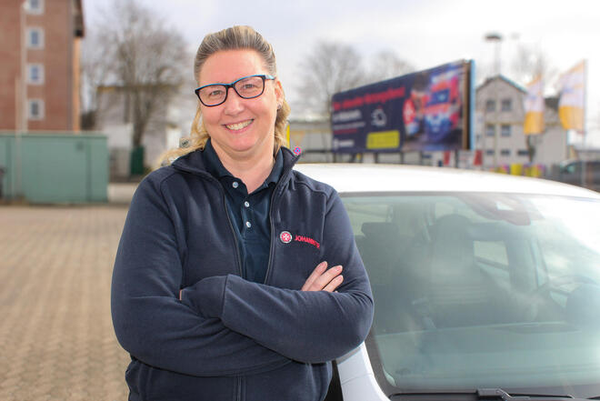 Eine Frau in einer Johanniter-Sweat-Shirt-Jacke vor einem weißen Auto