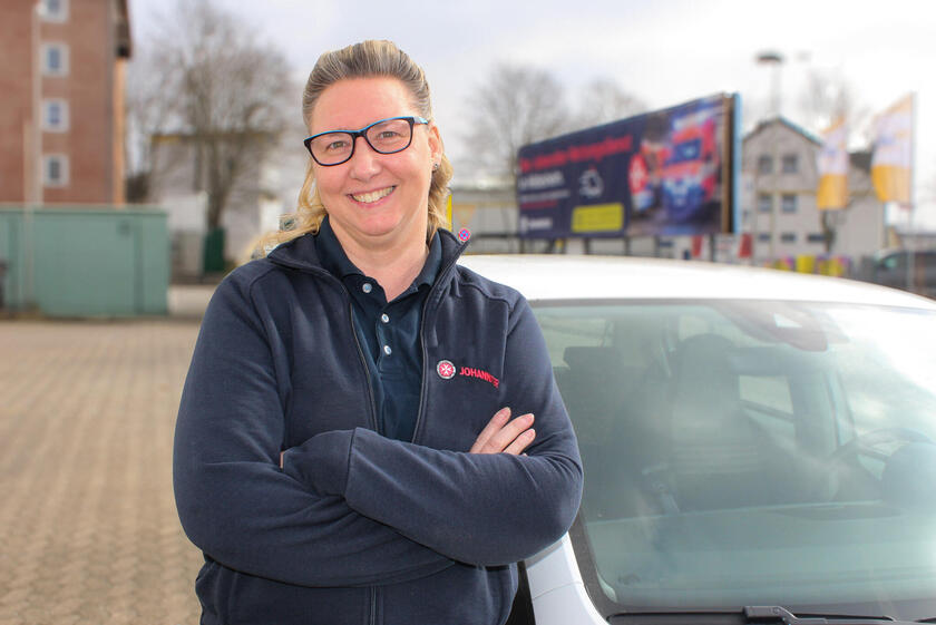 Eine Frau in einer Johanniter-Sweat-Shirt-Jacke vor einem weißen Auto