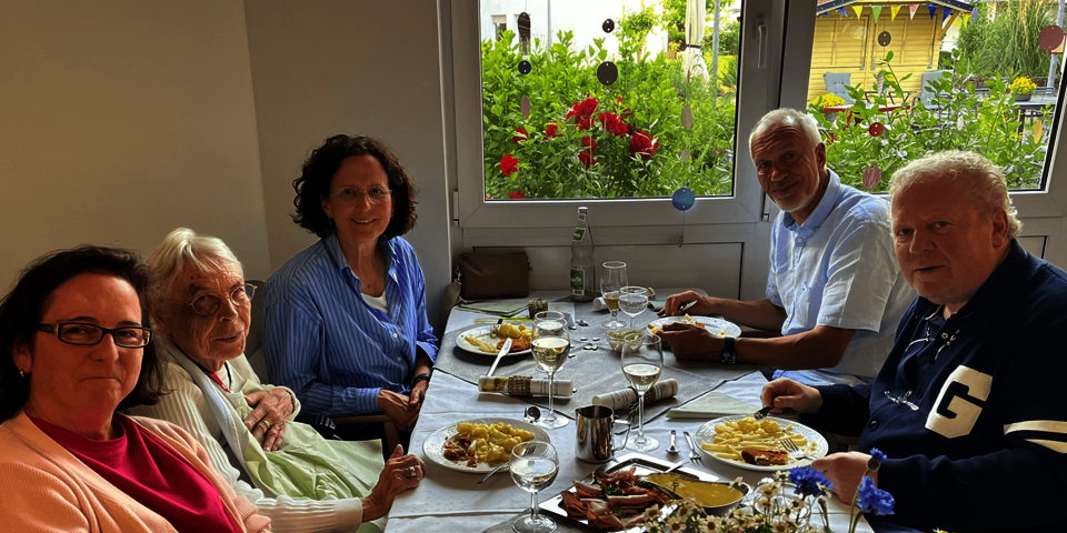 Fünf Personen unterschiedlichen Alters sitzen vor gefüllten Tellern an einem geschmückten Tisch