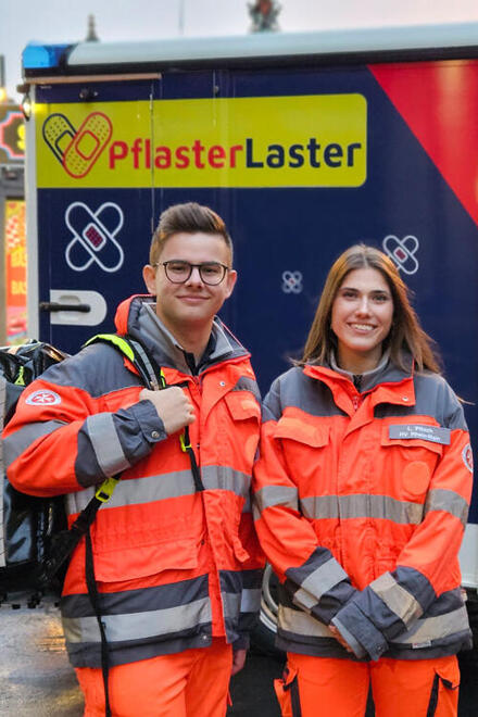 Ein Mann und eine Frau vor dem Johanniter-Pflasterlaster in Rettungsdienstkleidung
