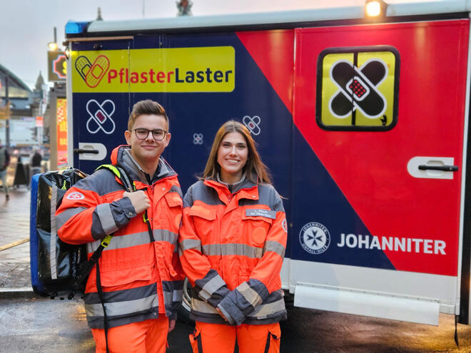 Ein Mann und eine Frau vor dem Johanniter-Pflasterlaster in Rettungsdienstkleidung