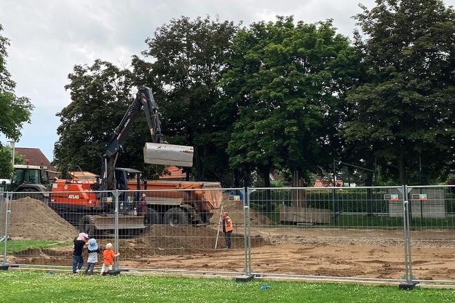 Kinder an einem Bauzaun, die einen Bagger beobachten