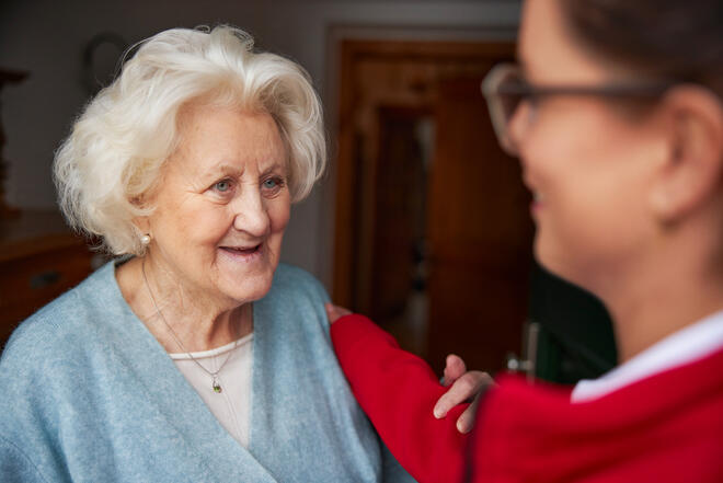Seniorin lächelt, jüngere Frau legt beruhigend die Hand auf ihre Schulter.