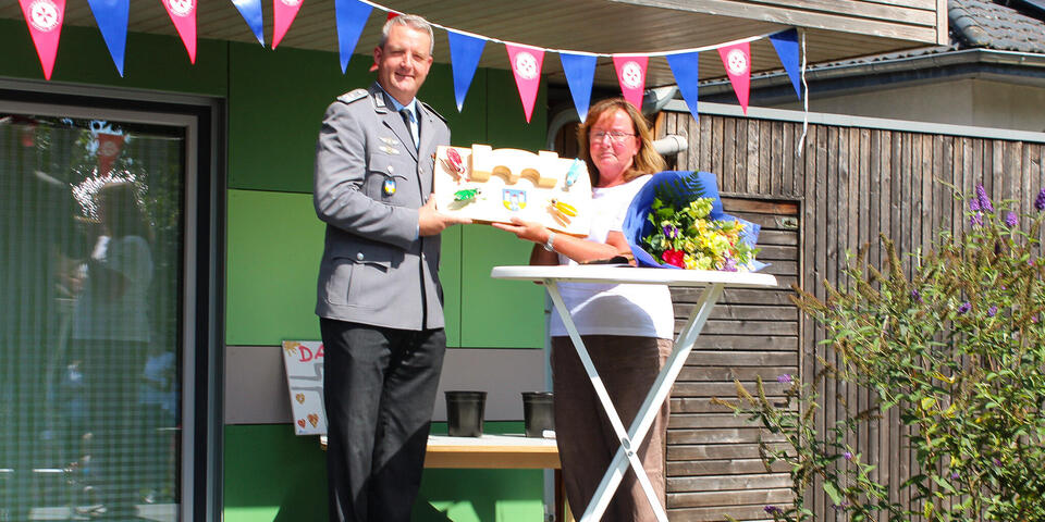 Ein Mann im Dienstanzug der Bundeswehr mit einem Schild, das er mit einer Frau hochhält