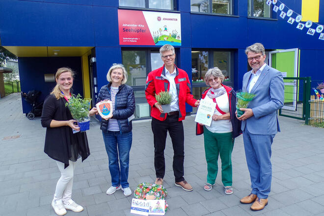 Johanniter-Kita Seehüpfer erhält Kneipp-Siegel Fünf Menschen stehen vor dem Gebäude der Kita und halten das Siegel, eine Urkunde sowie Kräuter in den Händen.