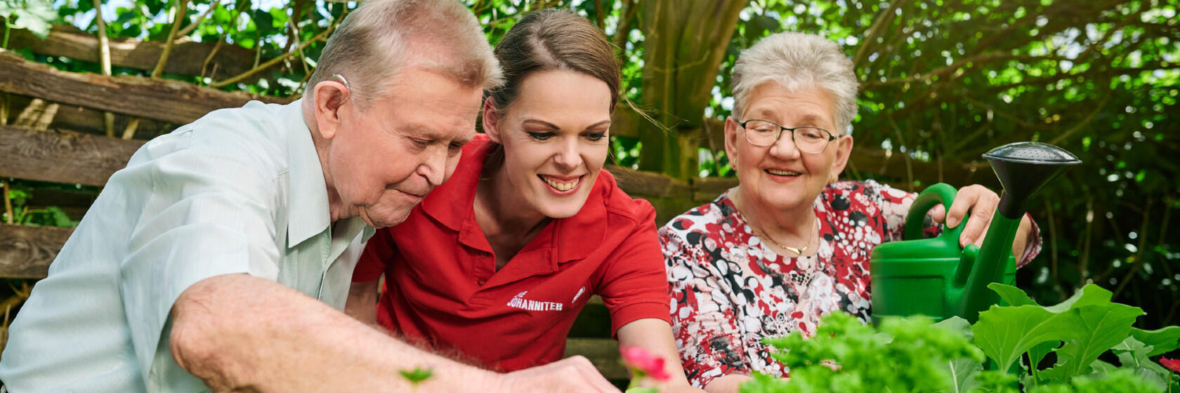 Eine Pflegerin der Johanniter ist mit zwei älteren Pflegepersonen im Garten.