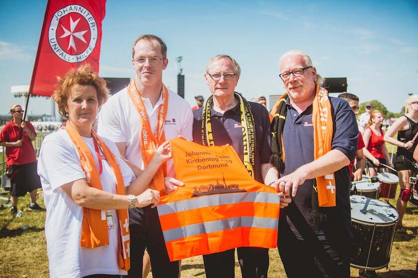 Vier Johanniter halten eine Warnweste in die Höhe