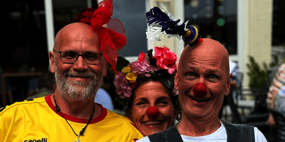 Zwei Männer und eine Frau mit roten Clownsnasen lachen in die Kamera.