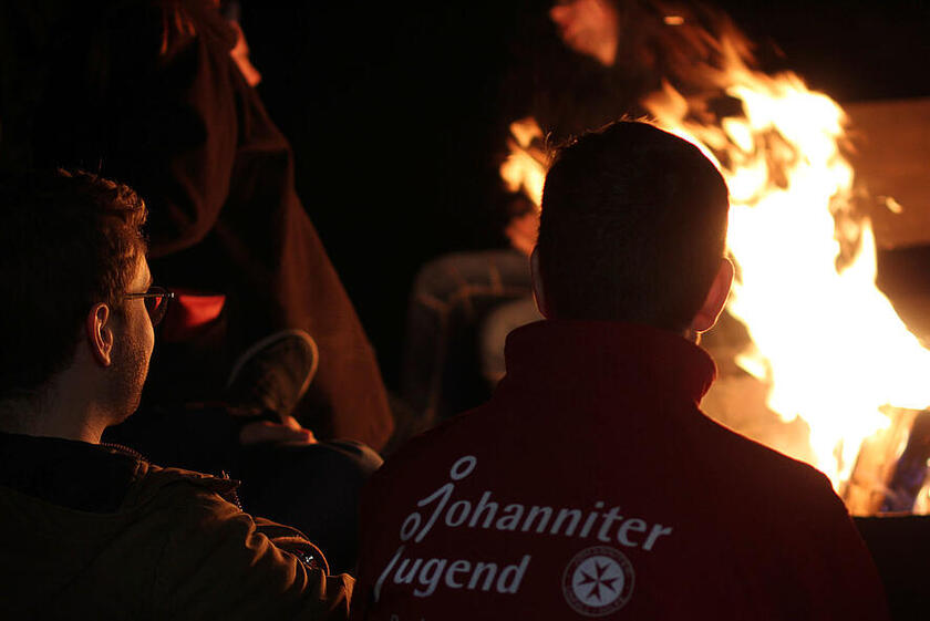 Zwei junge Menschen in Johanniter-Jugend-Kleidung sitzen an einem Lagerfeuer