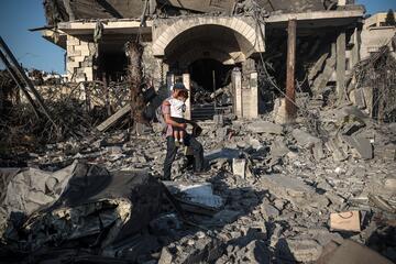 Mann mit Kleinkind auf dem Arm vor zerstörtem Haus.