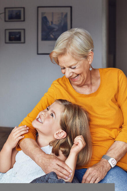 Eine Großmutter mit ihrer Enkelin. Die Oma trägt einen Hausnotruf-Sender am Handgelenk.