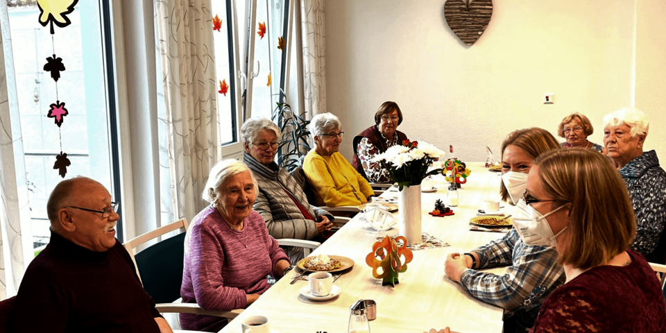 Ältere Menschen und Johanniter-Mitarbeiterinnen sitzen zusammen am Kaffeetisch