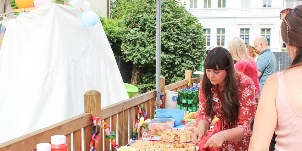 Ein Büffet mit verschiedenen Speisen. Eine frau im roten Kleid bedient sich.