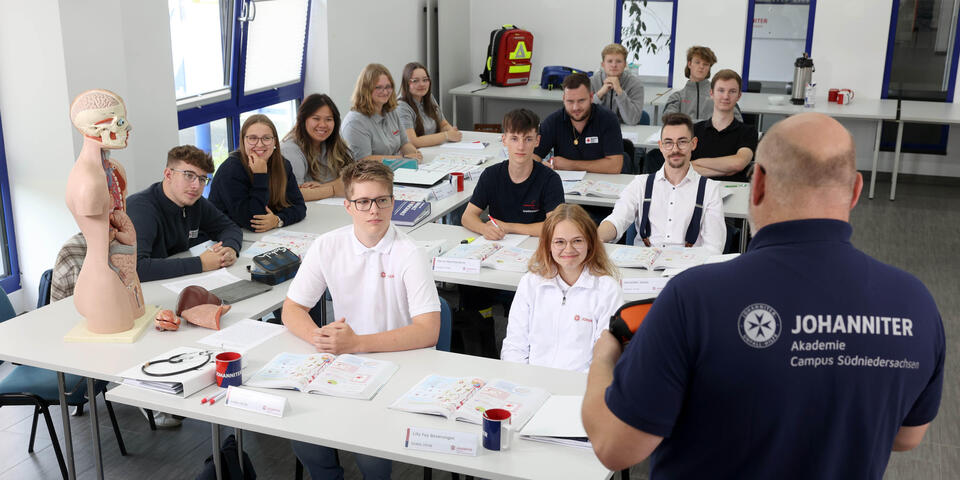 Mann steht vor einer Gruppe von jungen Menschen und unterrichtet sie