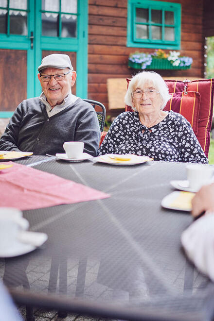 Ein älteres Paar sitzt an einem Tisch im Garten und lächeln