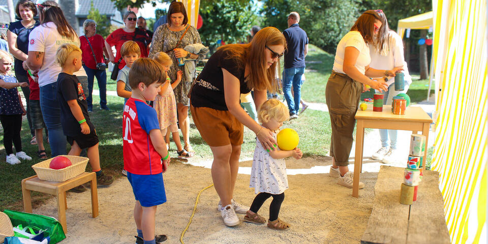 Eine Gruppe Kinder und Erwachsener unter einem Pavillon. Ein Kind hält einen gelben Ball
