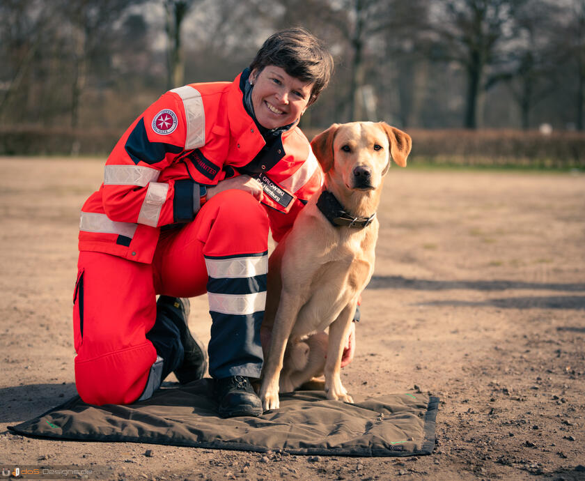 eine Ehrenamtliche der Rettungshundestaffel kniet neben ihrem Hund