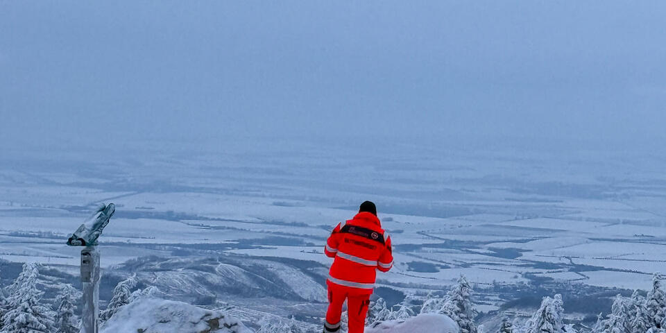 Ein Johanniter schaut von einem schneebedecktem Gipfel ins verschneite Tal