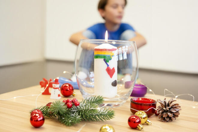 Unscharfer Junge im Hintergrund, vorn Weihnachtsdeko und leuchtende Kerze.