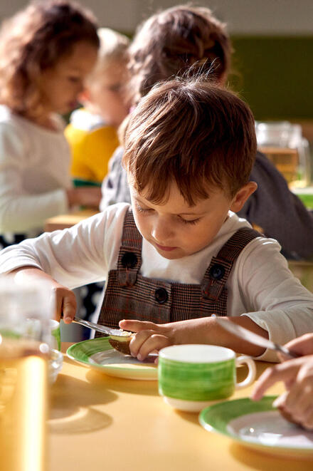 Ein Kind in einer KiTa schmiert sich ein Brot.