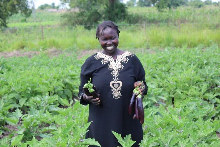 Für viele Geflüchtete bedeutet das Leben in Uganda die Chance auf einen Neuanfang Eine lächelnde Frau steht mit Auberginen in der Hand auf ihrem Feld