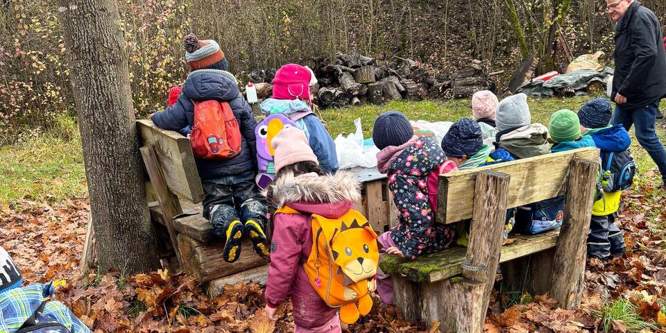 Kinder sitzen auf Holzbänken an einem Holztisch.