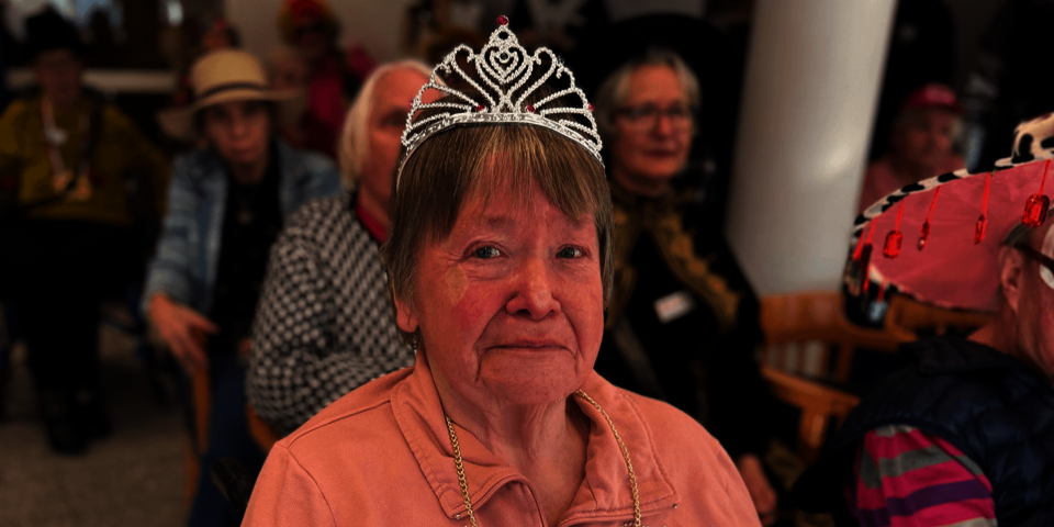 Frau mit glitzerndem Diadem; im HIntergrund sitzend weitere Menschen