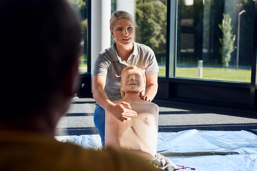 Eine Erste-Hilfe-Trainerin der Johanniter erklärt den Kursteilnehmenden die Wiederbelebungsmaßnahmen anhand einer Erste-Hilfe-Puppe.