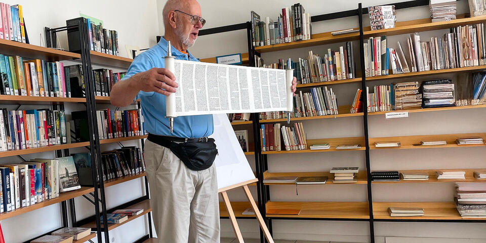Ein Mann in einer Bücherei hält eine Papierrolle mit Zeichen hoch
