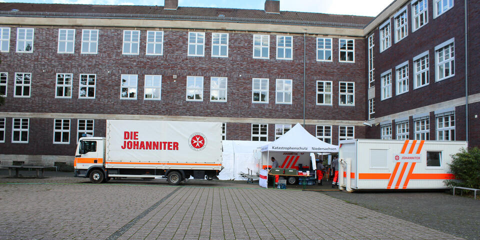 Ein Johanniter-LKZ ein Pavillon und andere Johanniter-Fahrzeuge vor einer Schule.