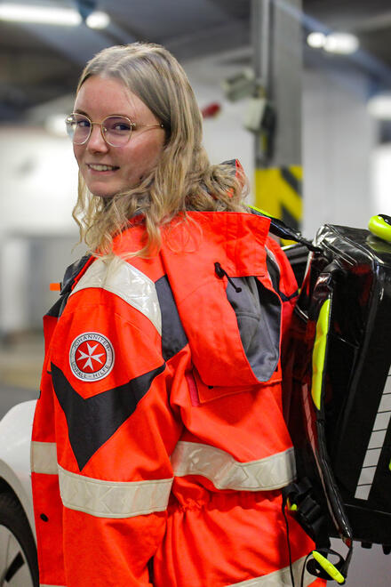 Eine junge Frau mit Johanniter-Bekleidung und einem Rettungsrucksack über der Schulter