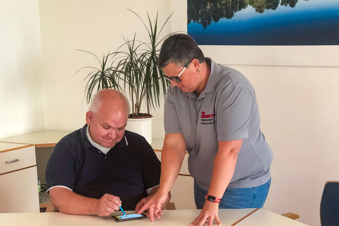 Eine Mitarbeiterin der Johanniter zeigt einem Kunden, wo auf dem mobilen Datenerfassungsgerät unterschreiben muss.