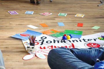 Materialien liegen auf dem Boden vertreut: ein Johanniter-Jugend-Banner, mehrere Pappkarten, Stifte