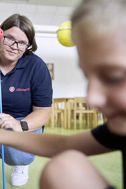 Eine Betreuerin der Johanniter beaufsichtigt ein spielerisches Konstruktionsprojekt in einer offenen Ganztagesschule. Ein Kind im Vordergrund konzentriert sich auf das Spiel.