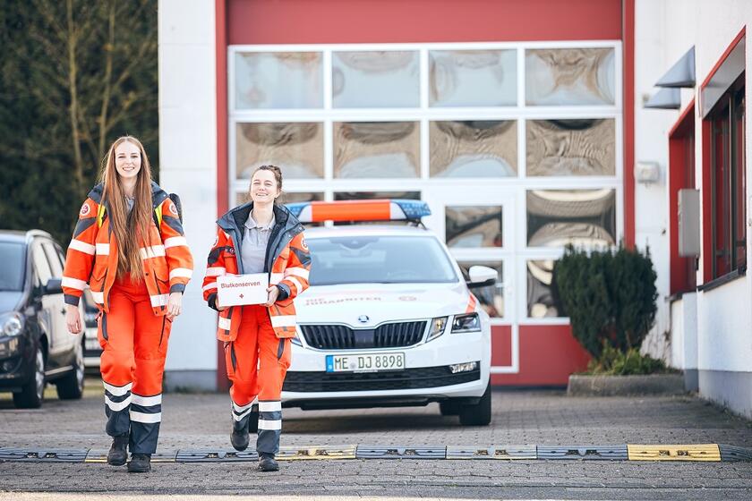 Zwei FSJlerinnen vor Johanniter-Fahrzeug, eine hält eine Transportbox für Blutkonserven in der Hand