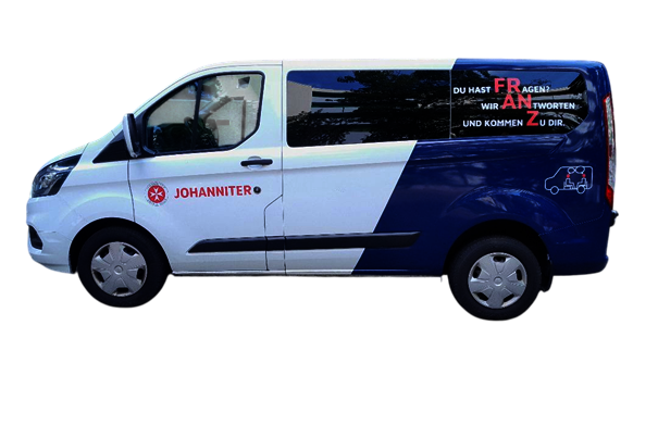 Ein weiß-blauer Transporter der Johanniter steht seitlich fotografiert. Auf der Vorderseite und der Fahrertür befindet sich das Logo der Johanniter und daneben der rote Schriftzug „JOHANNITER“. Auf dem hinteren Seitenfenster steht: „DU HAST FRAGEN? WIR ANTWORTEN. UND KOMMEN ZU DIR.“ Die Wörter „FRAGEN“ und „ZU“ sind dabei farblich hervorgehoben.