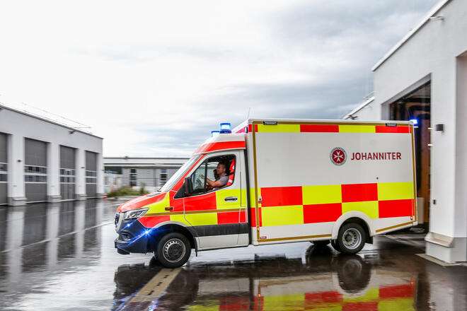 Johanniter-Rettungswagen fährt mit Blaulicht aus Garage.