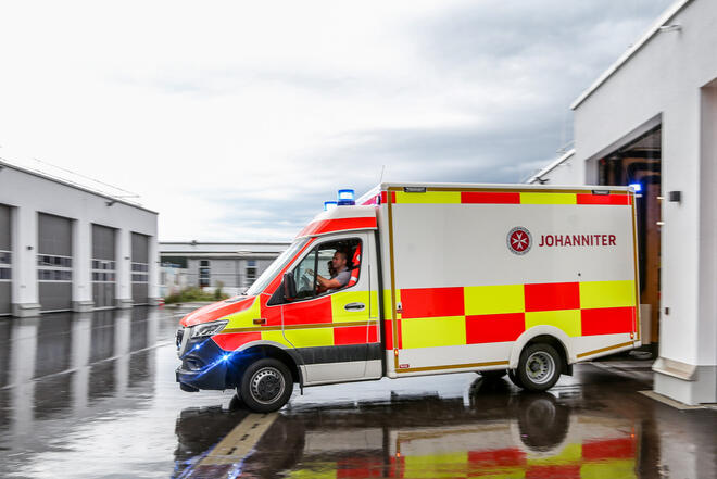 Johanniter-Rettungswagen fährt mit Blaulicht aus Garage.
