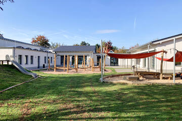 Ein Außengelände einer Kita mit Klettergerüsten, einem Sandkasten und darüber Sonnensegel