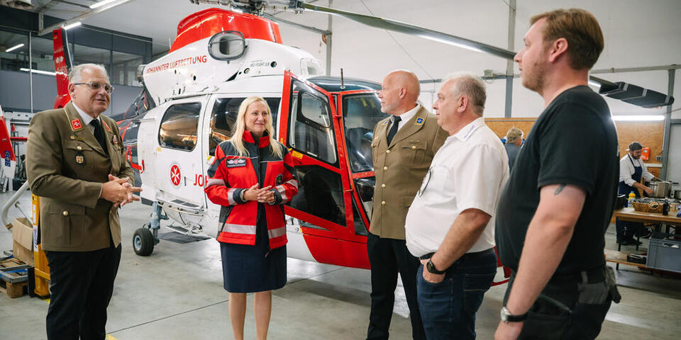 Staatsministerien trägt eine Rettungsdienst-Jacke. Im Gespräch mit Geschäftsführer Meermann und anderen im Hangar der JLR.