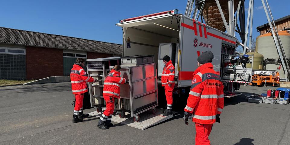 Johanniter schieben Rollcontainer in einen Gerätewagen