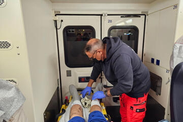 Mann in Rettungsdienstkleidung behandelt die Beine eines Patienten in einem Rettungswagens