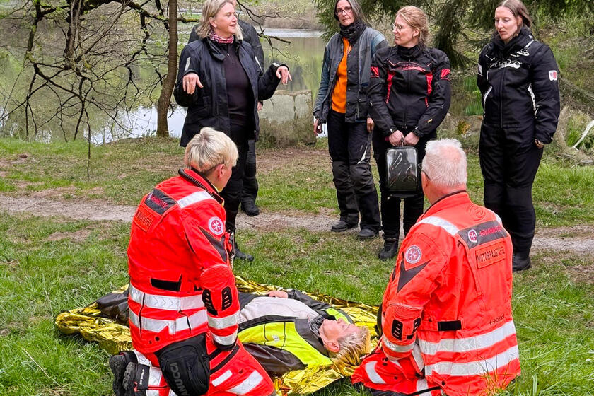 Johanniter knien neben einer Person, andere Menschen schauen zu