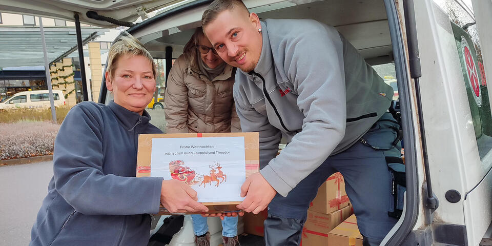 Eine Frau reicht ein Paket mit einem liebevollem Gruß einem Johanniter in ein Fahrzeug.