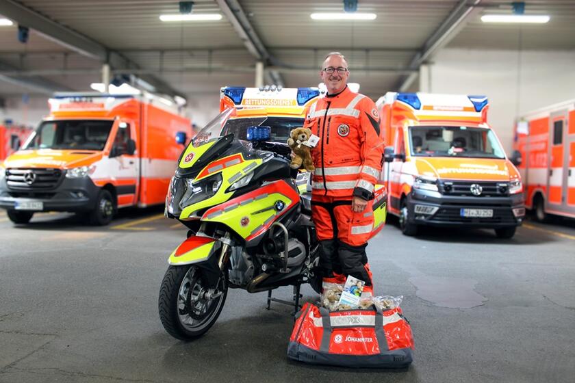 Ein Mann mit seinem Motorrad und Trösteteddy steht vor drei Einsatzwagen